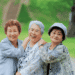 Three elderly women smiling and embracing each other in a green park.