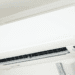 White wall-mounted air conditioner unit with its front panel closed and vent opening visible on the lower front edge.