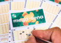 Close-up of Brazilian Mega-Sena lottery cards on a table, with a hand marking numbers with a pen.