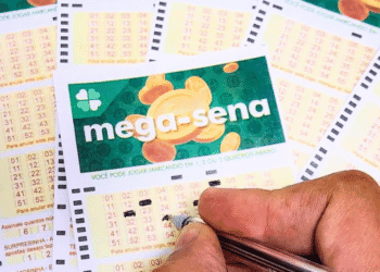 Close-up of Brazilian Mega-Sena lottery cards on a table, with a hand marking numbers with a pen.