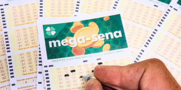 Close-up of Brazilian Mega-Sena lottery cards on a table, with a hand marking numbers with a pen.