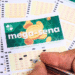 Close-up of Brazilian Mega-Sena lottery cards on a table, with a hand marking numbers with a pen.