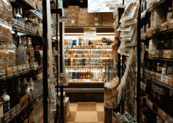 A narrow supermarket aisle with shelves stocked full of bottled drinks and a refrigerated section at the end.