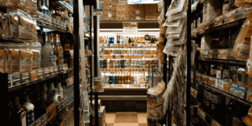 A narrow supermarket aisle with shelves stocked full of bottled drinks and a refrigerated section at the end.