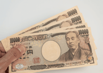 Salário mínimo em Aichi pode subir novamente primeira reunião sobre reajuste é realizada - ThingsOut Hand holding a fan of Japanese 10,000 yen banknotes featuring Yukichi Fukuzawa.