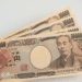 Hand holding a fan of Japanese 10,000 yen banknotes featuring Yukichi Fukuzawa.