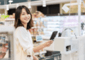 Takaichi deve avançar com corte temporário no imposto sobre alimentos no Japão - ThingsOut Smiling woman at a grocery store checkout paying with her smartphone at the payment terminal.