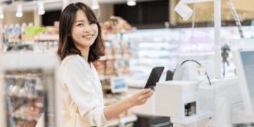 Smiling woman at a grocery store checkout paying with her smartphone at the payment terminal.