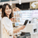 Smiling woman at a grocery store checkout paying with her smartphone at the payment terminal.