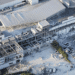 Aerial view of a damaged mall with collapsed roof and debris scattered in the parking lot, AEON Mall signage visible on the building path nearby.