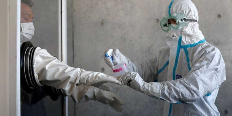 Profissional de saúde desinfecta luvas de colega em Tosuka, ao sul de Tóquio