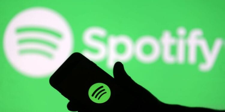 A smartphone is seen in front of a screen projection of Spotify logo, in this picture illustration